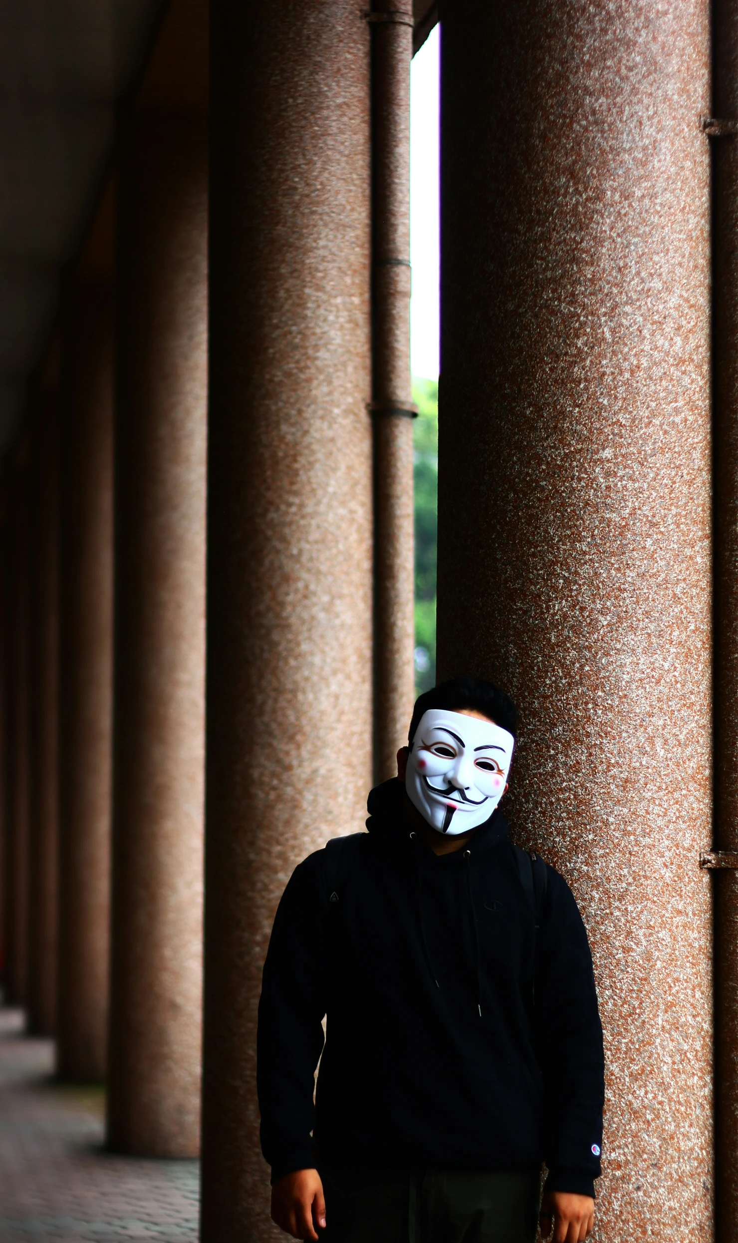 a man stands in an alley next to tall columns with his face painted on it