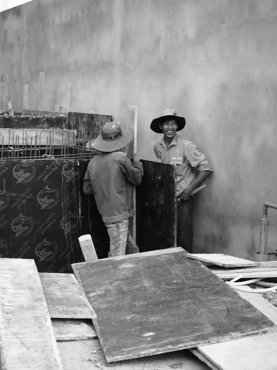 two men standing next to an unfinished piece of wood