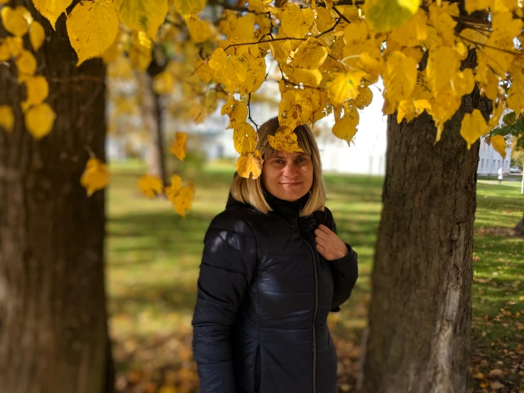 a woman in a black jacket is standing between some trees