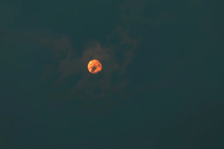 a yellow moon appears in the cloudy dark sky