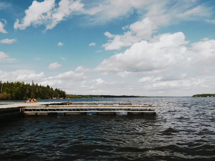 the pier in the middle of the lake has a row of picnic tables on it