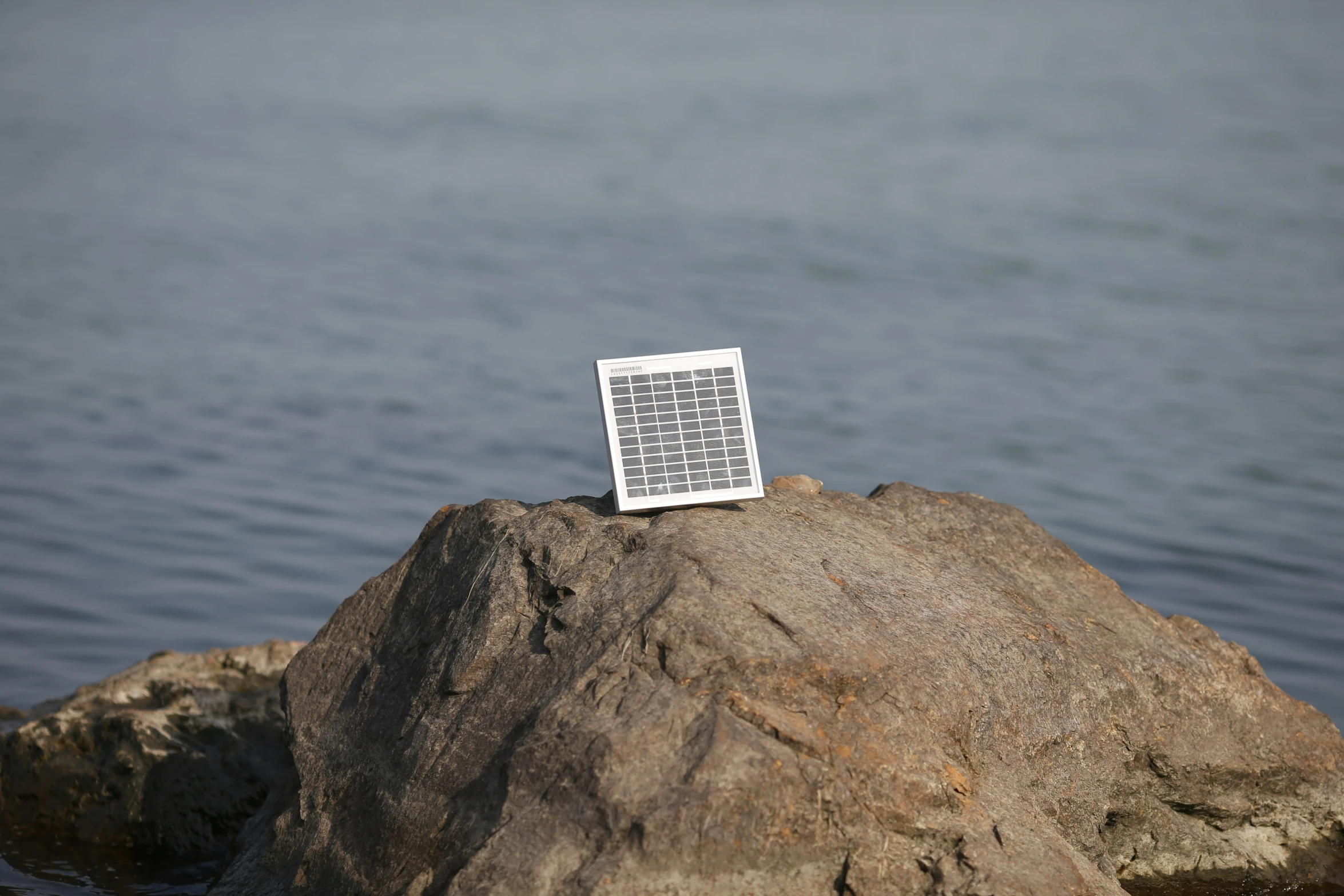 a keyboard laying on top of a rock by the water