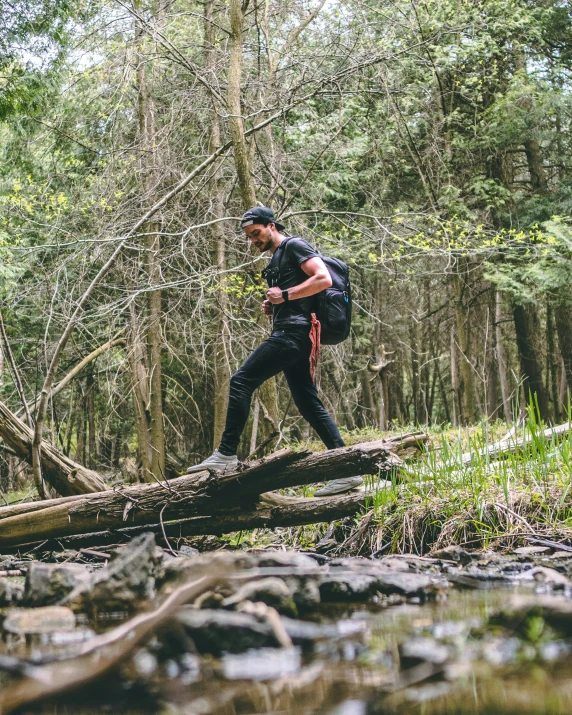 man with backpack walking over fallen log in forest