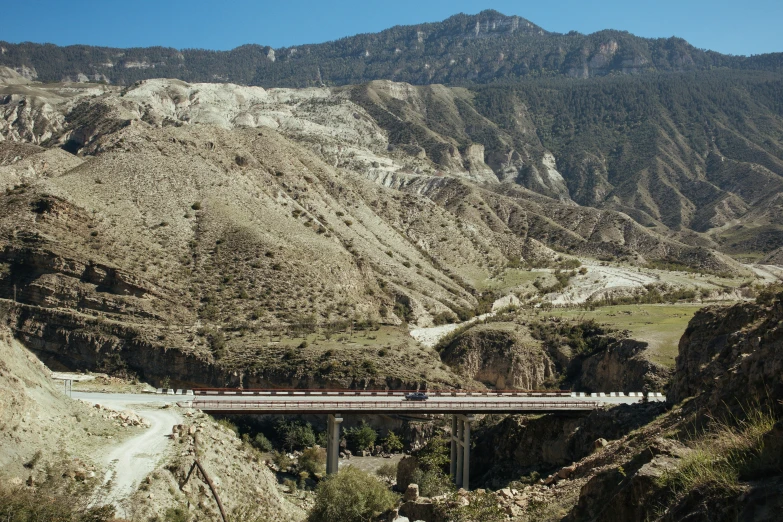 a train is going over a bridge that stretches over a cliff into mountains