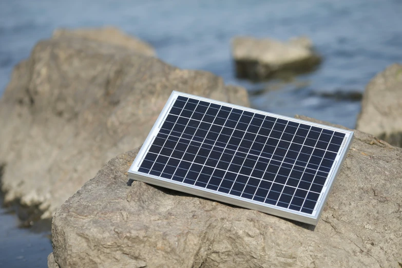 there is a solar panel on a rock by the water