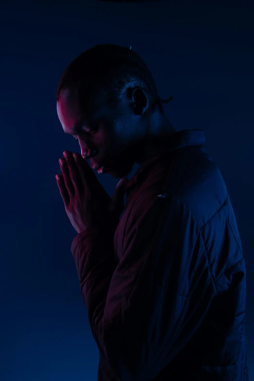 a person in dark clothes stands against a blue background