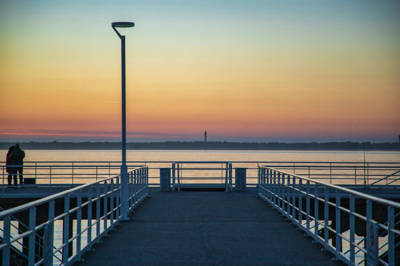 the walkway to the water at dusk with a person standing on the end