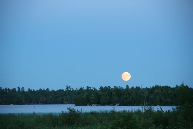 an moon rising over a lake by the woods