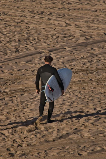 a man walking across a sandy beach holding a surfboard