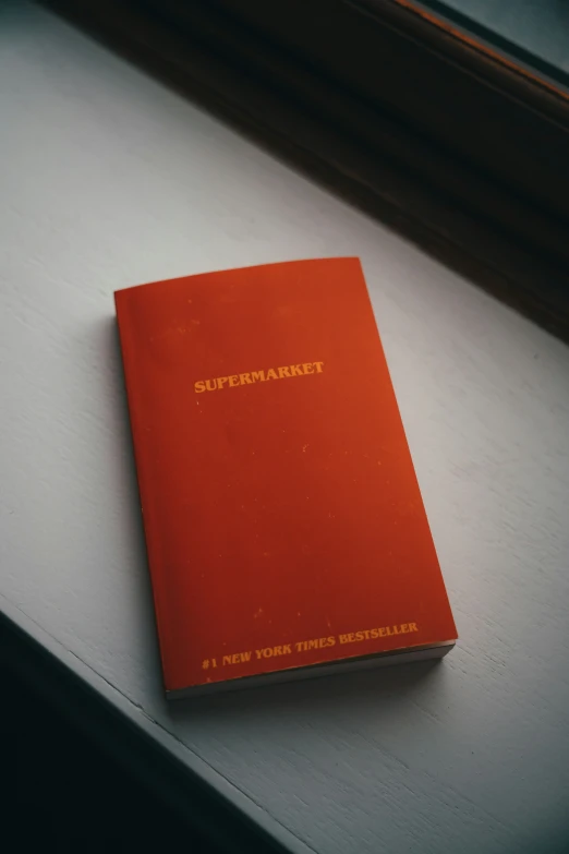 a red book with words written on it sitting on a window sill