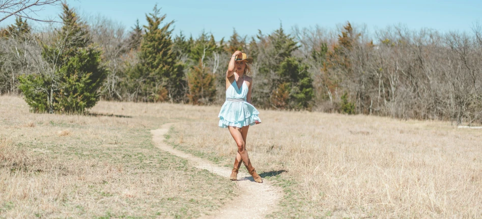 woman in dress standing on dirt road in grassy field