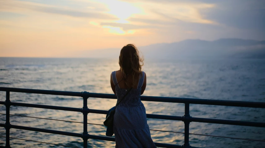 a woman standing on the side of a bridge in front of a body of water