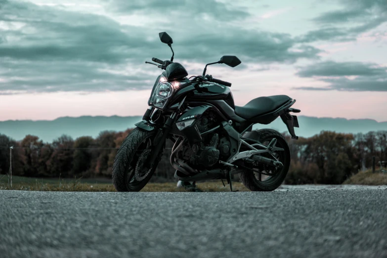 black motorcycle sitting on asphalt near field and cloudy sky