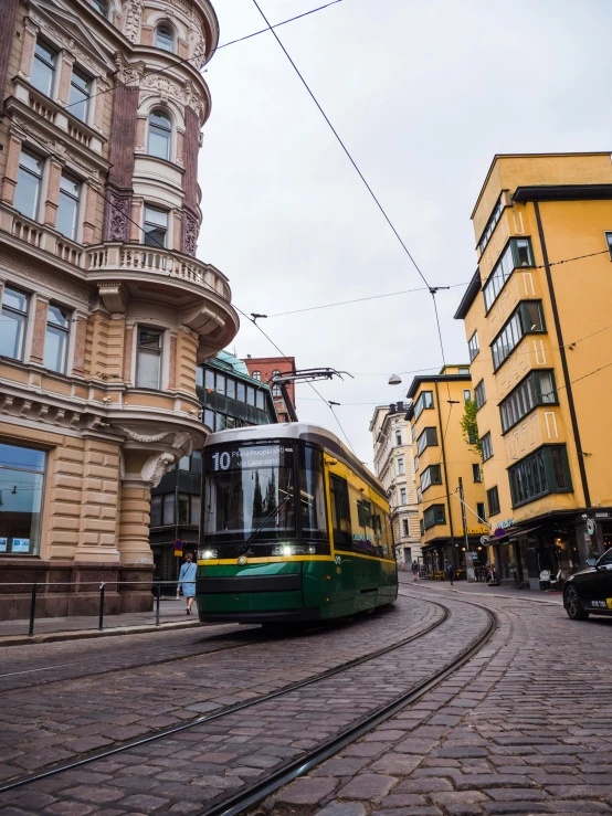 a yellow and green bus moving along some buildings
