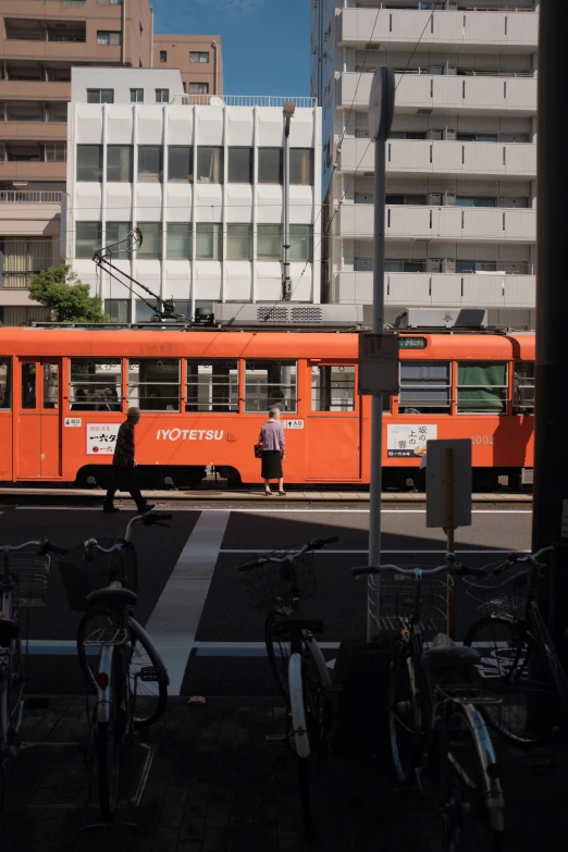 an orange street car is going by many bikes