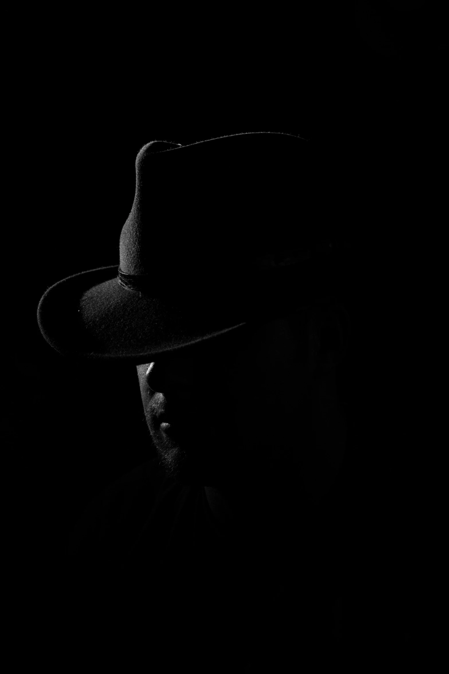 black and white image of a man in the dark with a hat on