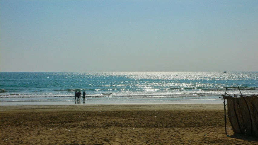 a couple stand on the beach next to a fence and looking out to sea