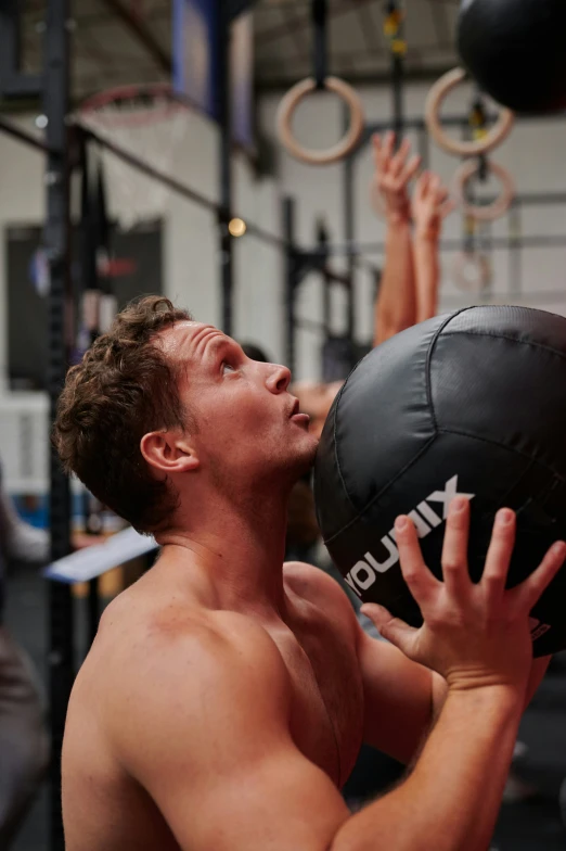 a shirtless man lifts a medicine ball over his shoulder
