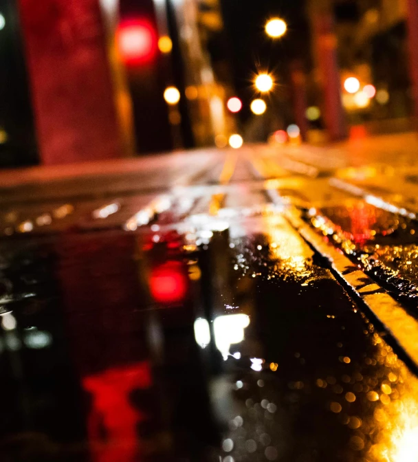 a wet street is lit by the red traffic lights