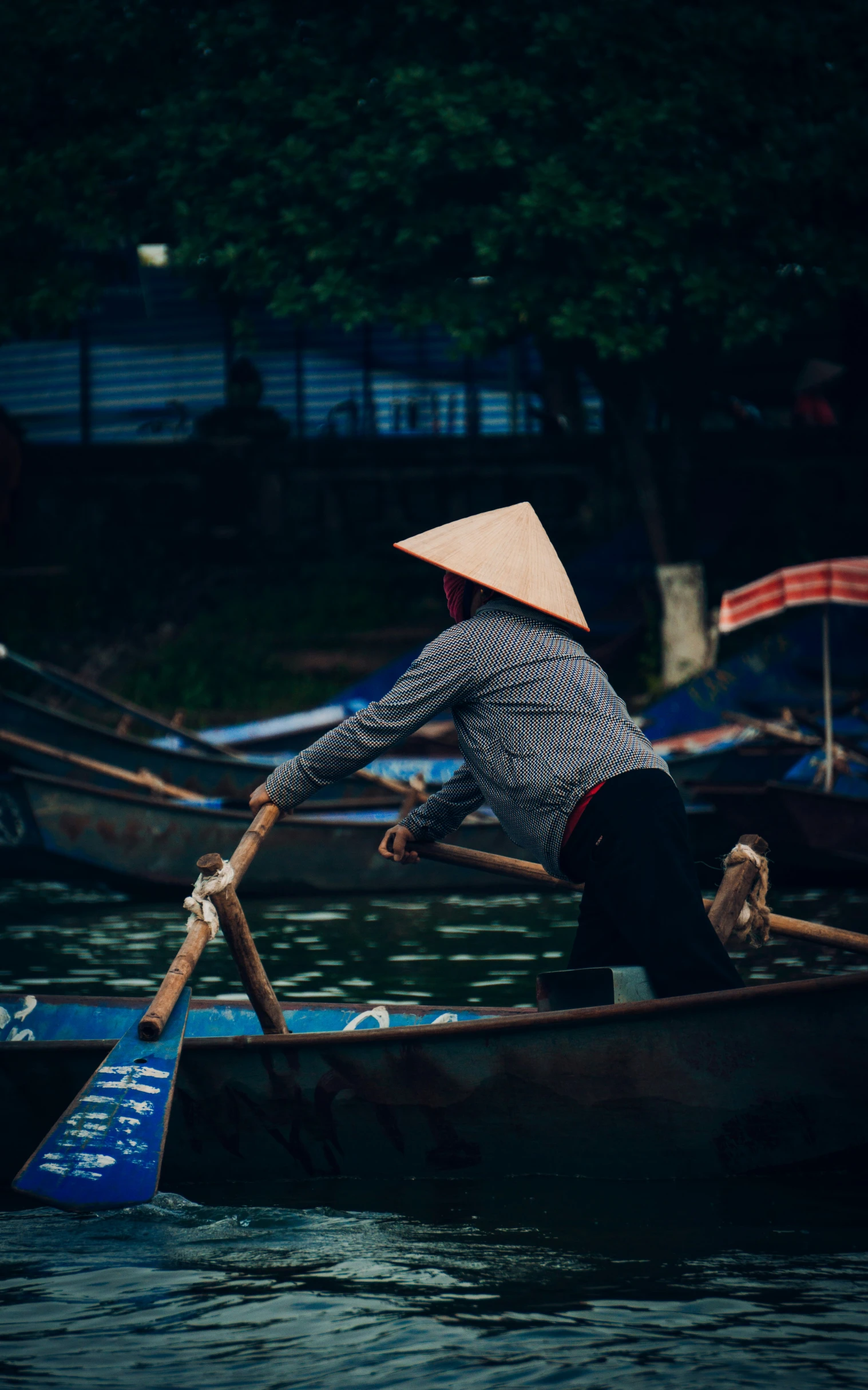 woman on a boat paddles through water with trees and buildings behind her