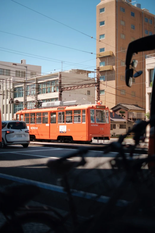 an orange streetcar traveling down a street past tall buildings