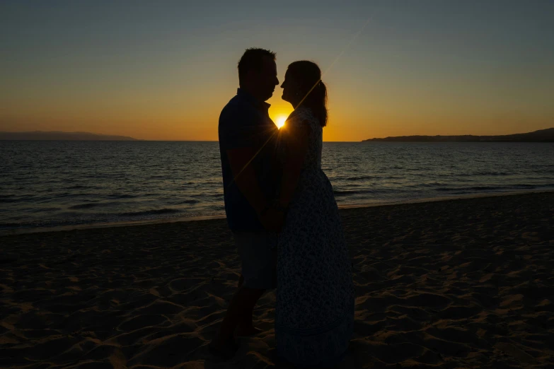 a couple standing on the beach during sunset