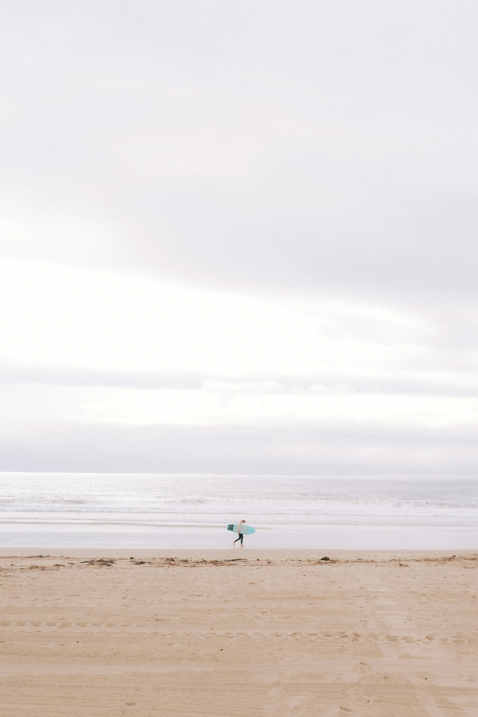 a man standing on the sand of the beach holding a surfboard