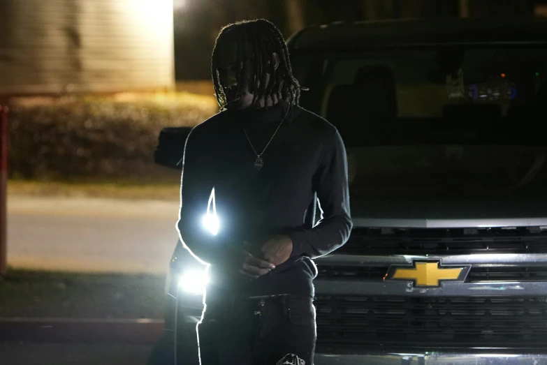 a person in black and a black sweatshirt and hoodie, standing outside at night