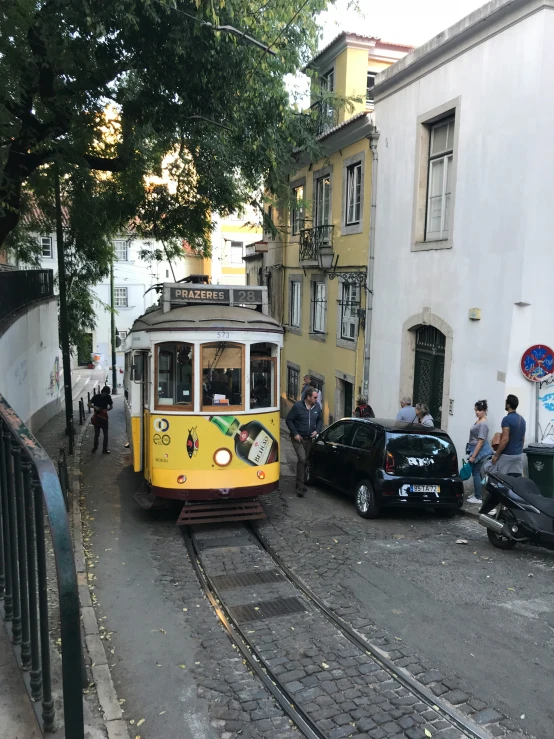 yellow train on street and people sitting outside