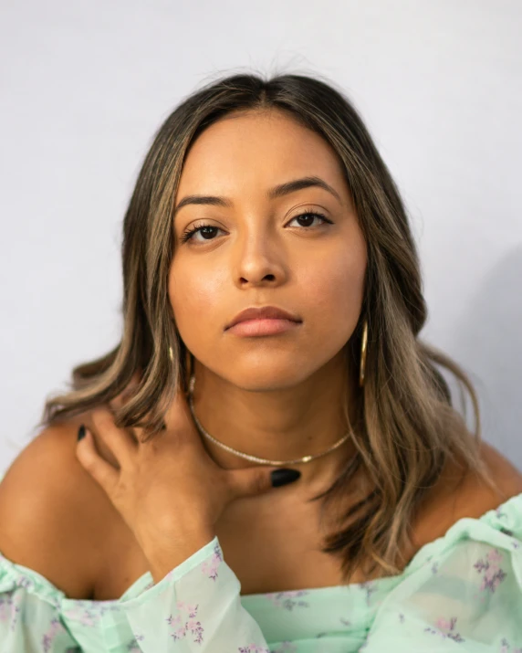 a woman wearing an off the shoulder dress with a hand on her chin