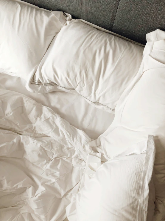 an unmade bed with white sheets and pillows