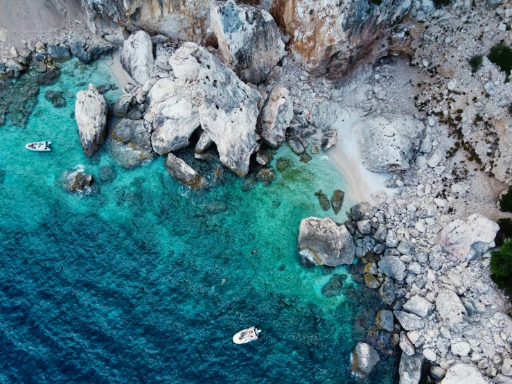 several boats anchored in a blue sea near rocky coastline