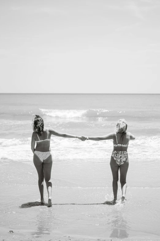 two women are on a beach holding hands