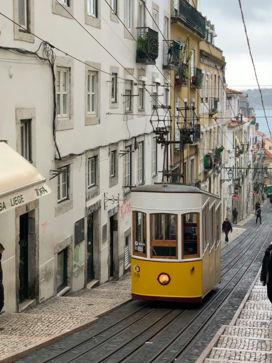 a yellow tram traveling up the hill between buildings