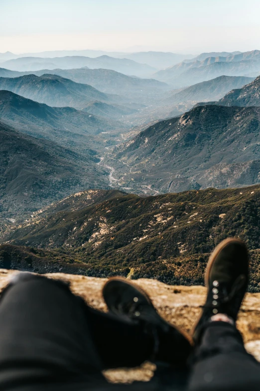 someone is sitting on a mountain looking at a valley