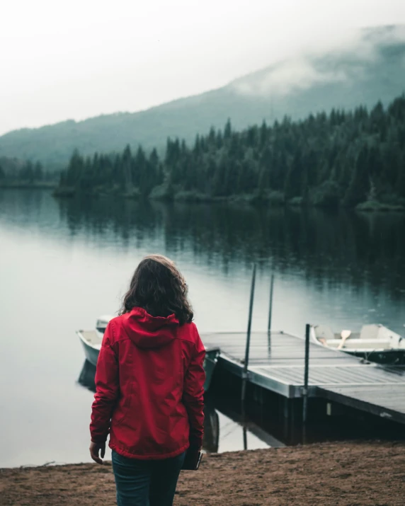 a person stands by the lake, looking at the boat