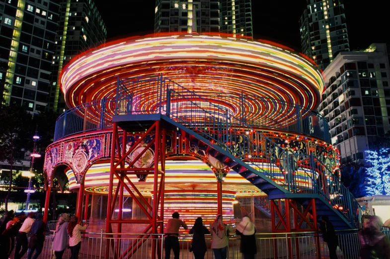 people walk near a carousel in an illuminated city