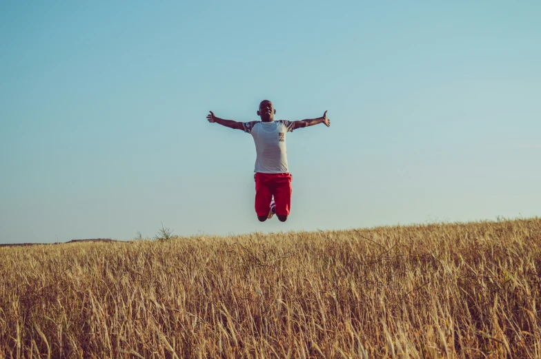 the man is jumping in a field with his arms wide out