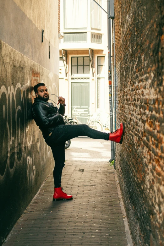 a man wearing red shoes leaning against a wall