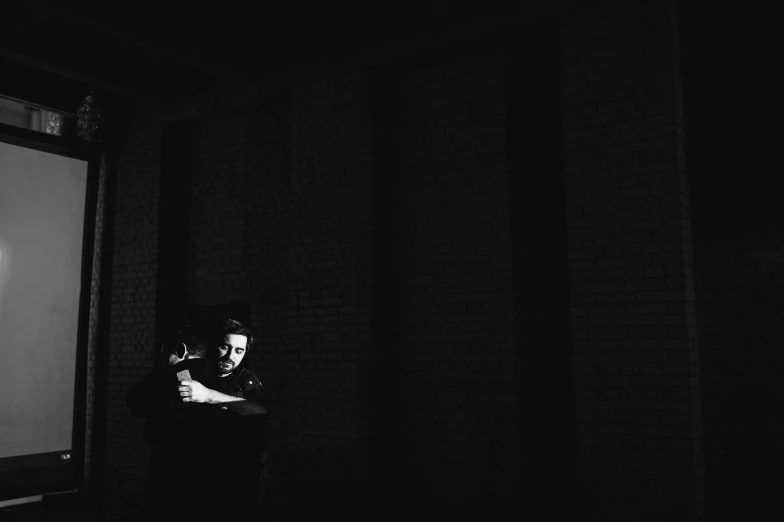 man with gun looking out of window at light in dark room