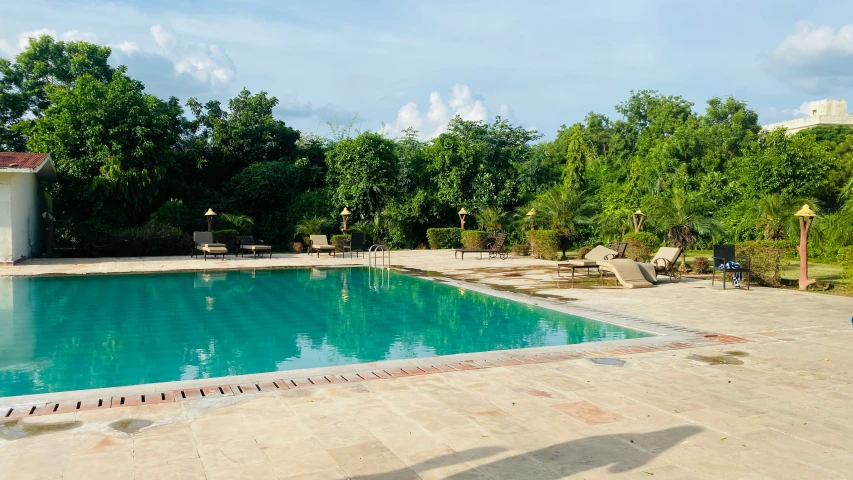 a long pool is seen surrounded by trees and furniture