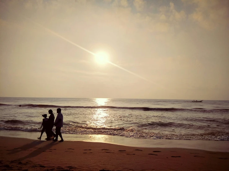 two people are walking along the beach as the sun rises