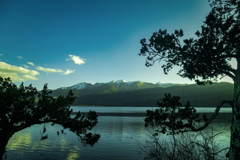 the view of a lake from the shore with mountains in the background