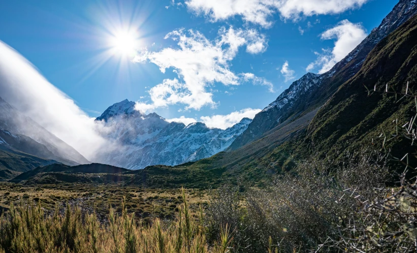 a green valley surrounded by mountains under a blue sky with clouds