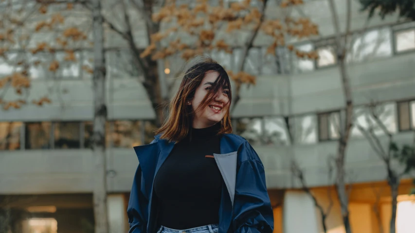 a woman in a black sweater and blue jacket standing in front of trees