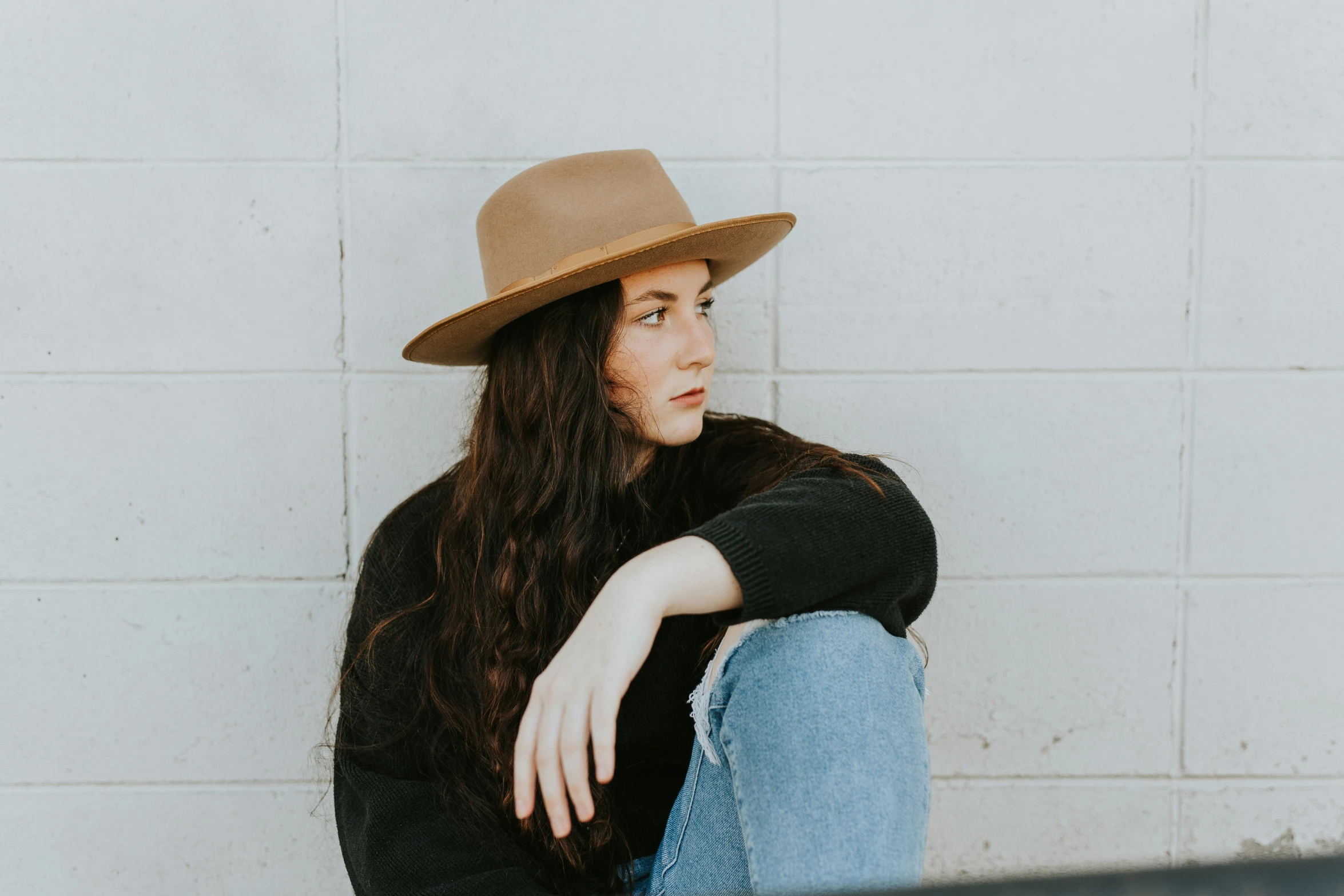 a woman with a hat and jeans sits down