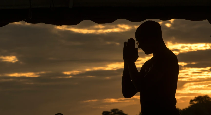 a silhouette of a person praying at sunset