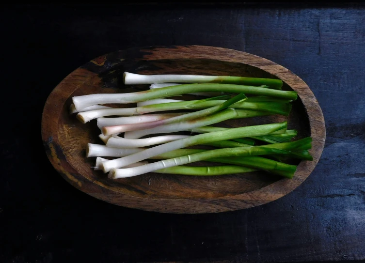 green onions and leeks in a bowl on a wooden surface