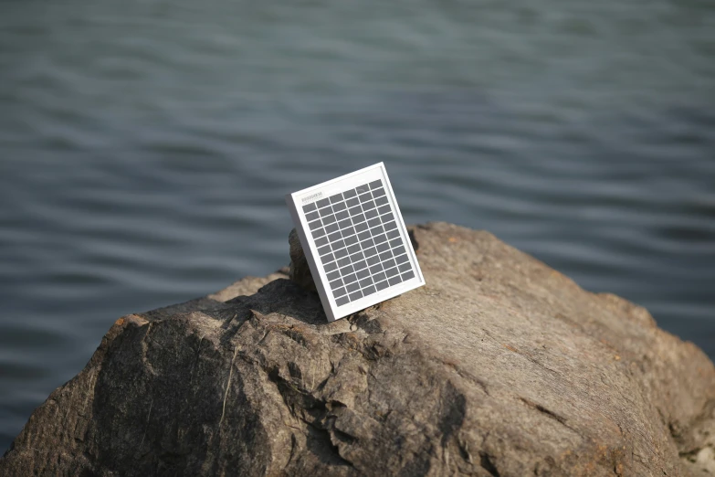 a small computer keyboard sitting on a rock near water