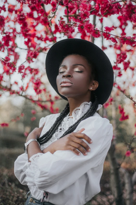 woman in a black hat, white shirt and blue jeans posing in front of a red tree